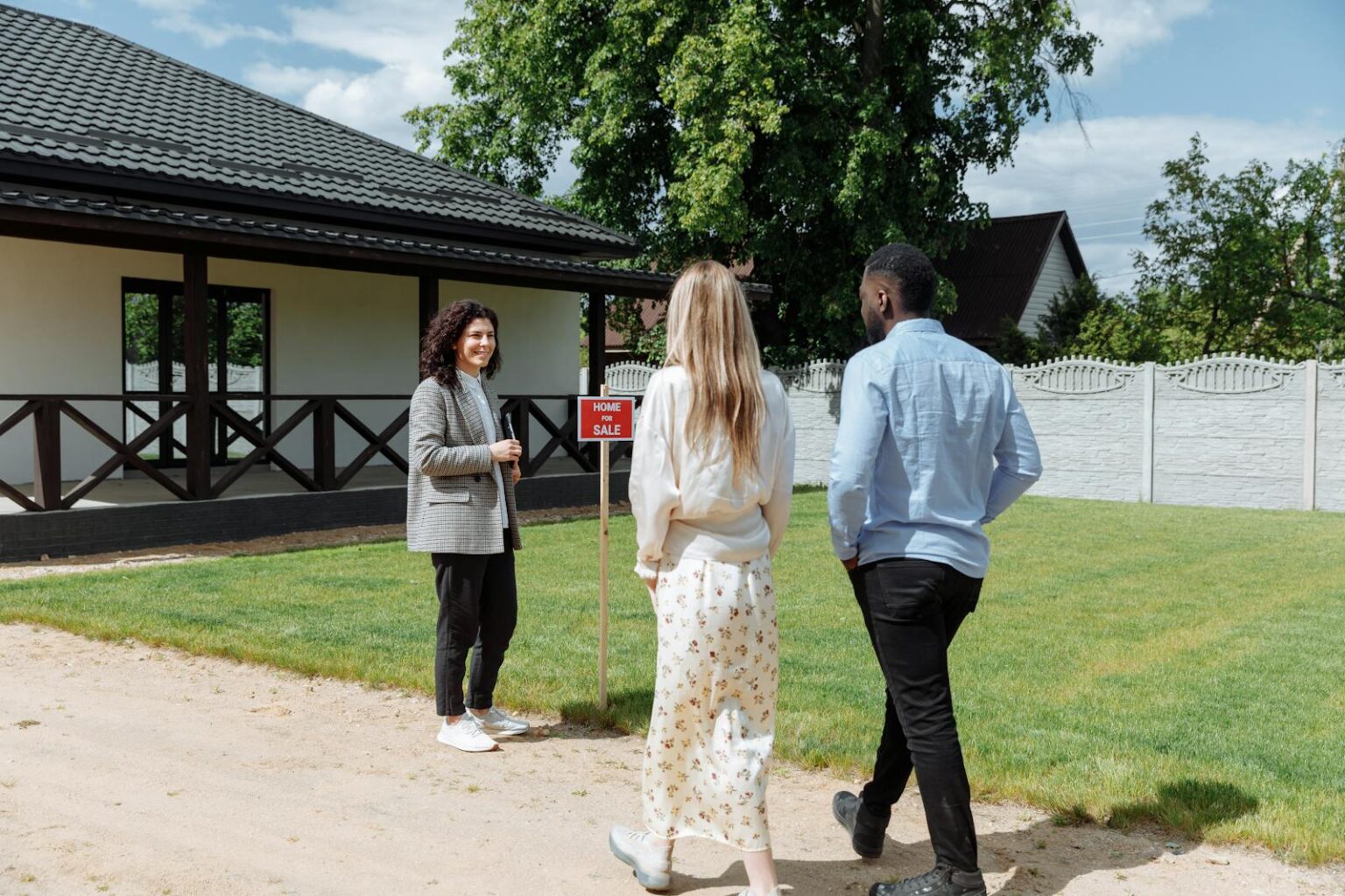 A diverse group viewing a house for sale with a real estate agent outdoors.